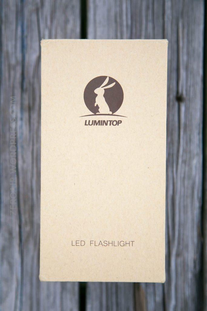 A rectangular cardboard box labeled “LUMINTOP” with a rabbit logo and the words “LED FLASHLIGHT” printed below, placed on a wooden surface.