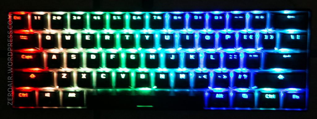A mechanical keyboard with backlit keys displaying a gradient of colors from red on the left to green in the center and blue on the right. The keys are illuminated and the keyboard is photographed from above.