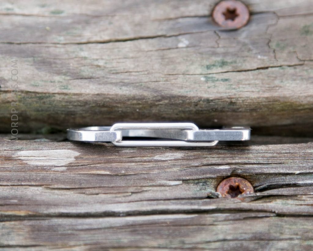 A silver metal object with a rectangular loop rests horizontally on weathered wooden planks secured with rusty screws.