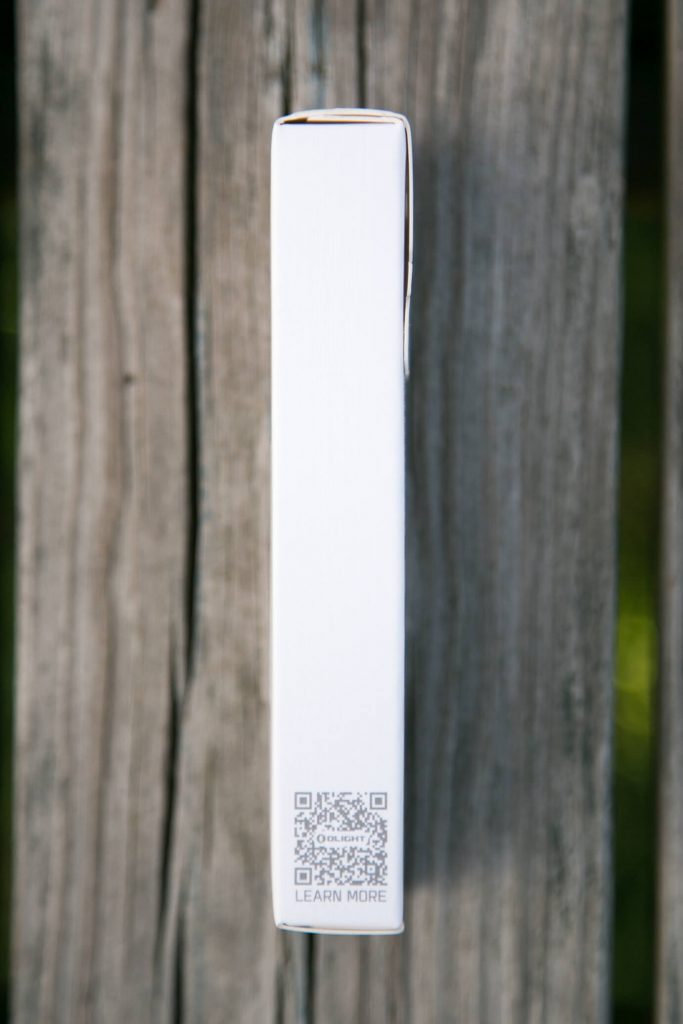 A white rectangular box with a QR code and the words LEARN MORE printed near the bottom, photographed vertically against a weathered wooden background.