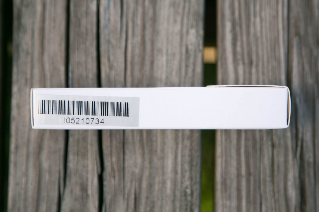 A white box features a black barcode and the number 05210734 printed below it, resting on a weathered wooden surface with visible grain and gaps between the planks.