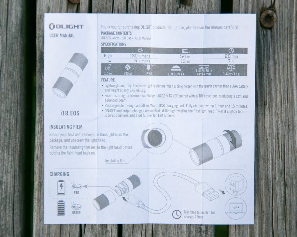 A printed user manual for the Olight i1R EOS flashlight, showing product specifications, operation instructions, a diagram, and charging details, resting on a wooden surface.