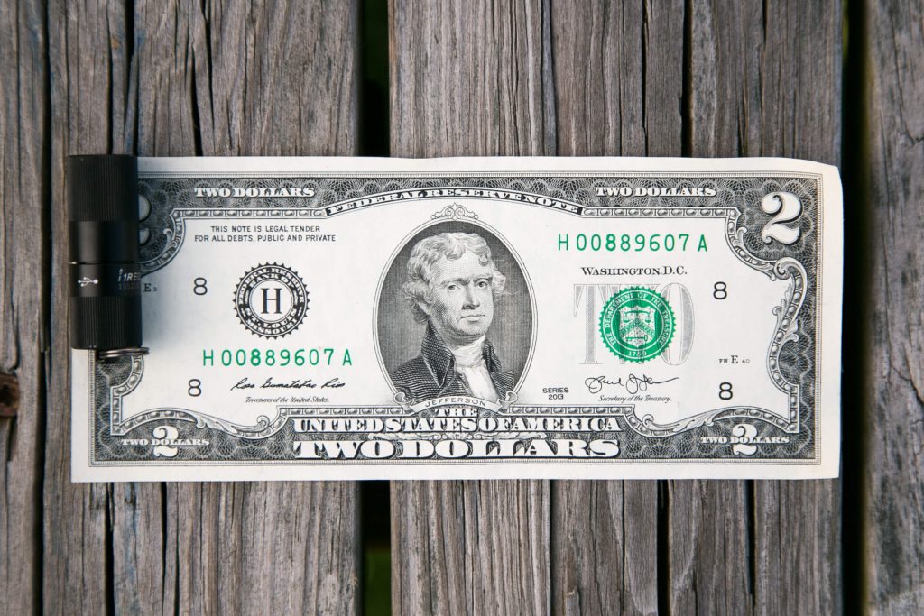 A two-dollar U.S. bill clipped to a wooden surface with a black binder clip, showing Thomas Jeffersons portrait and bill details clearly.