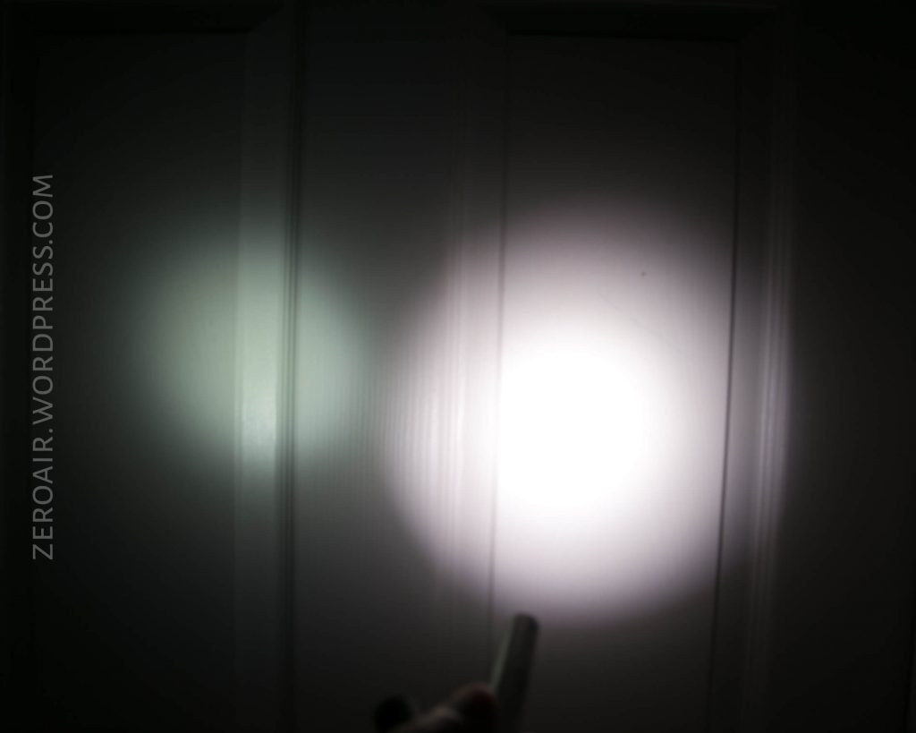 A flashlight beam is shining on a white paneled door in a dark room. The beam creates a bright circular spot with softer edges and some light spill to the left. Text reading ZEROAIR.WORDPRESS.COM is visible on the left side.