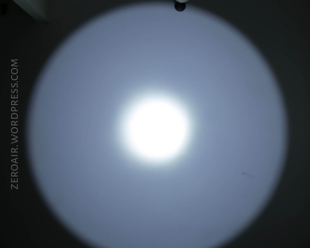 A circular beam of white light projected onto a smooth, grey surface, fading at the edges. The watermark “ZEROAIR.WORDPRESS.COM” is vertically visible on the left side.
