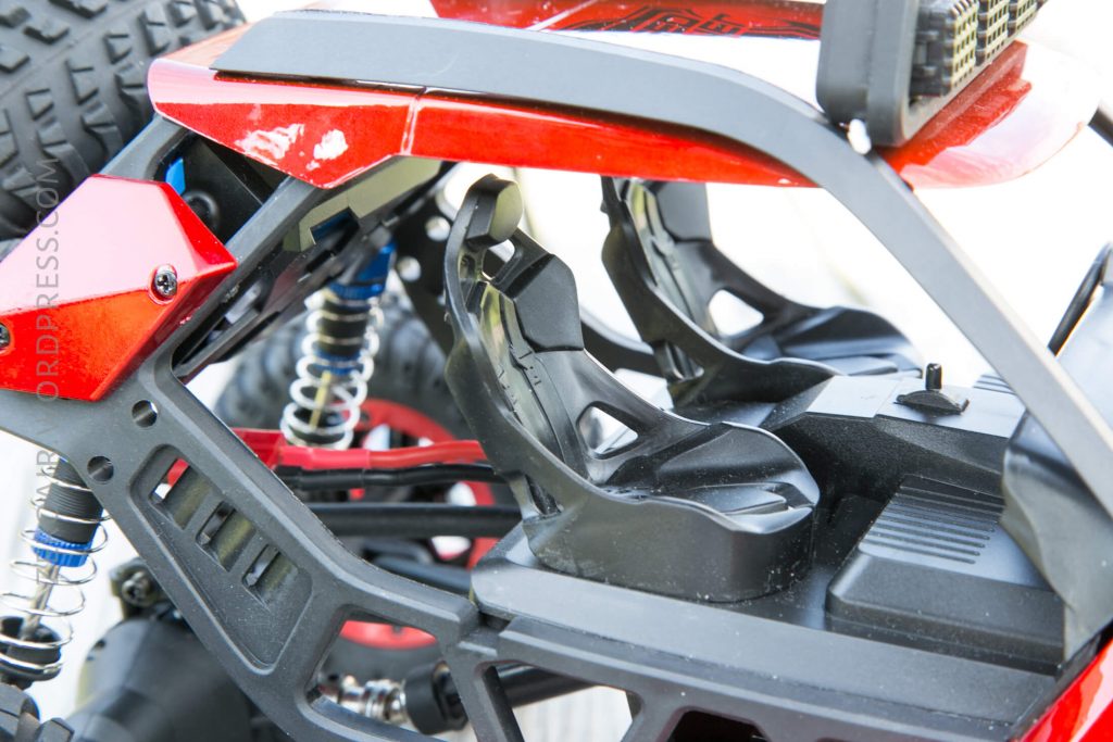 Close-up view of the interior of a red remote-controlled car, showing two black plastic racing-style seats, suspension springs, and part of the vehicles chassis.