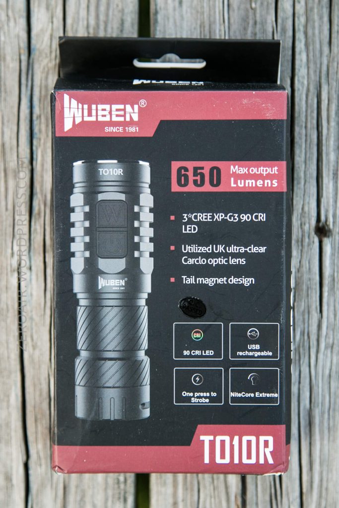 A black and red product box for the Wuben TO10R flashlight is shown on a wooden surface. The box highlights 650 max output lumens, 90 CRI LED, USB rechargeable, and other product features.