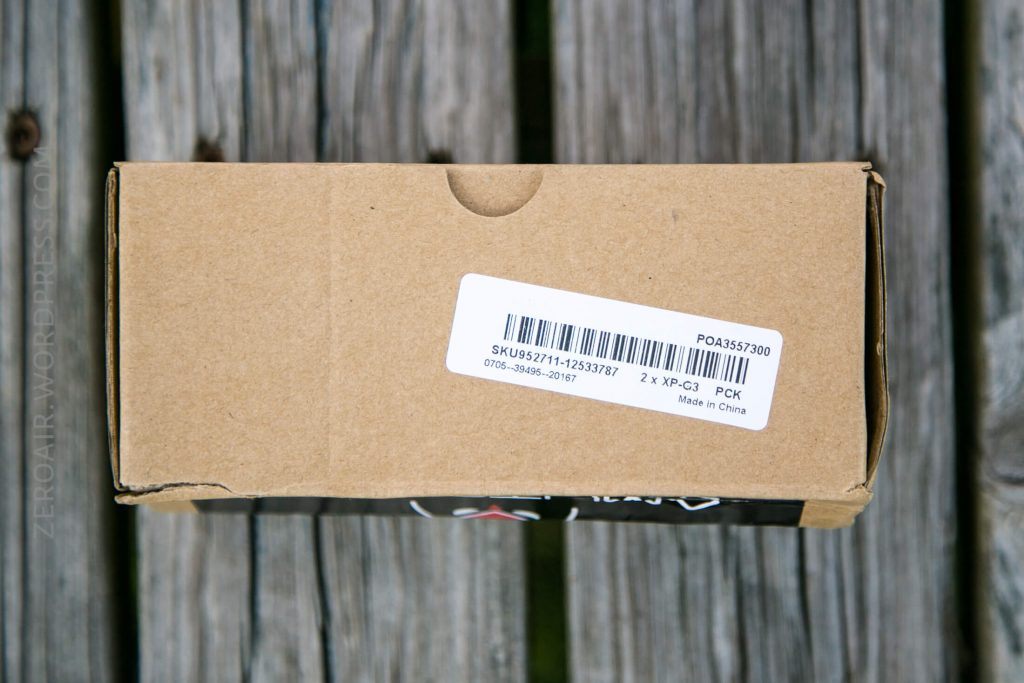 A brown cardboard box with a white barcode label attached on top, placed on a wooden surface. The label includes barcodes, SKU numbers, and text indicating it is made in China.