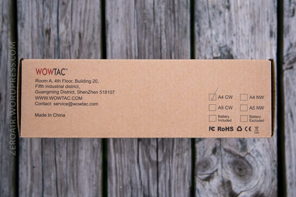 A brown WOWTAC product box sits on a wooden surface. The box displays company information, model options with A4 CW checked, and icons indicating battery status, certifications, and “Made in China.”