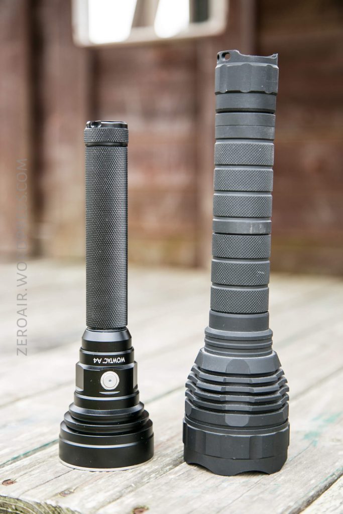 Two black flashlights stand upright on a wooden surface. The flashlight on the left is shorter and slimmer, while the flashlight on the right is taller and has a thicker, textured grip.