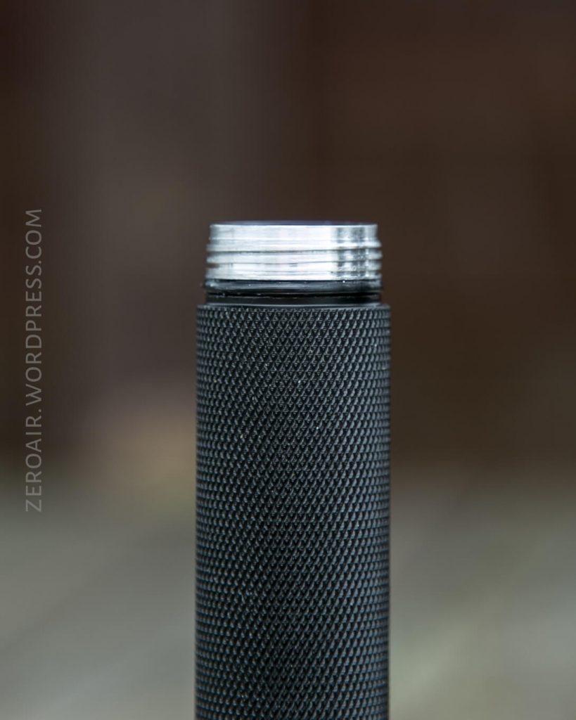 A close-up of a cylindrical black object with a textured grip and exposed silver threads at the top, positioned vertically against a blurred brown background. The text ZEROAIR.WORDPRESS.COM is visible on the left side.