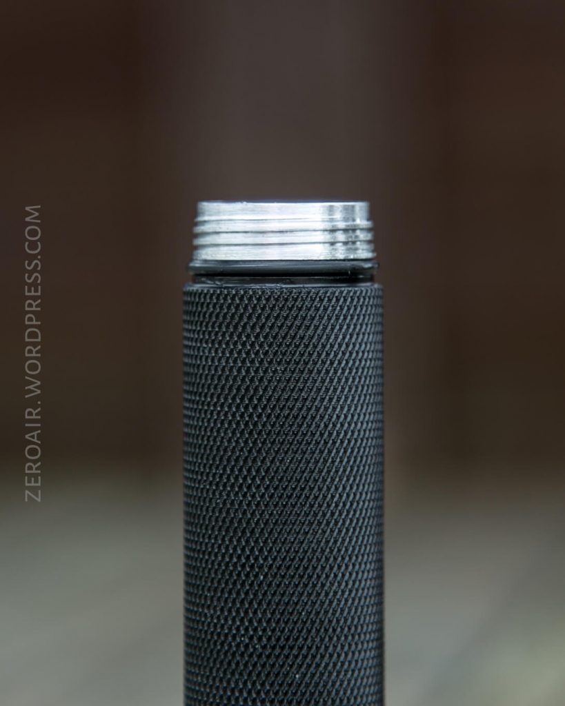 A close-up of a cylindrical, textured black metal object with visible silver threading at the top, shown against a blurred brown background. The text ZEROAIR.WORDPRESS.COM appears vertically on the left.