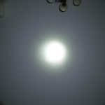 A bright circular spotlight is projected onto a plain wall with a ceiling light fixture partially visible at the top. The words ZEROAIR.WORDPRESS.COM are along the left side.