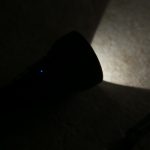 A flashlight is shining a beam of light onto a textured surface in a dark setting. The flashlight itself is mostly in shadow. zeroair.wordpress.com is written vertically along the left side.