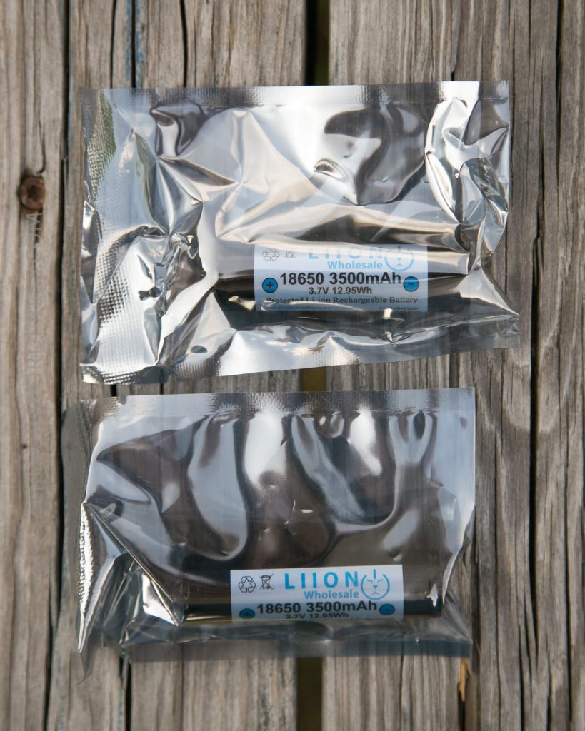 Two silver vacuum-sealed packages containing cylindrical lithium-ion batteries labeled “18650 3500mAh 3.7V 12.95Wh” rest on a wooden surface.