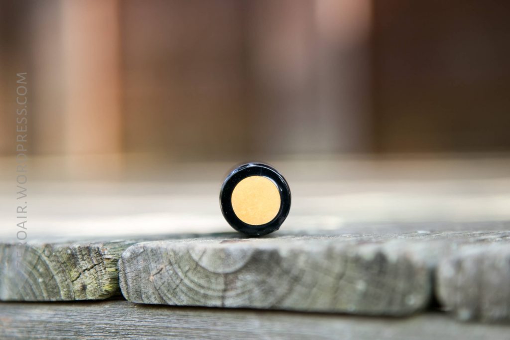 A small, round container with a yellow substance inside sits on a weathered wooden surface. The background is blurred, drawing focus to the container.
