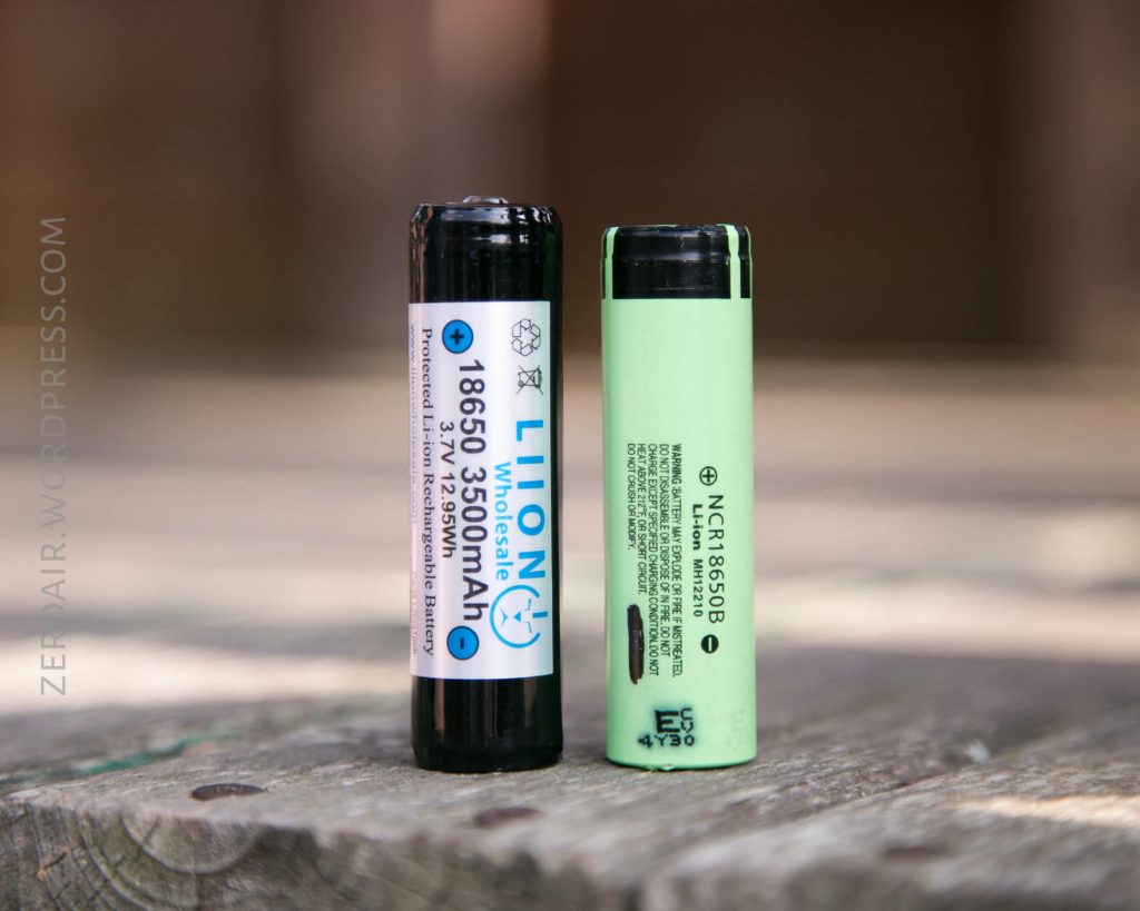 Two cylindrical 18650 lithium-ion batteries stand upright on a wooden surface, one black with a label showing 3500mAh, the other light green with black printed text and a barcode.