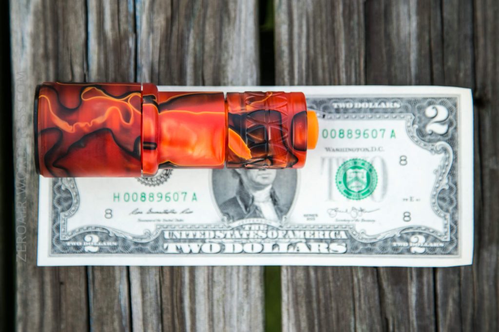 A red and orange patterned flashlight is placed horizontally on top of a U.S. two dollar bill, which is lying flat on a weathered wooden surface.