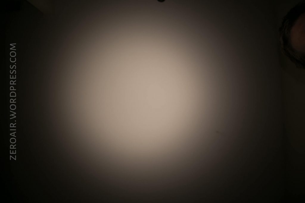 A circular beam of light shines on a dark surface, creating a gradient effect. The text ZEROAIR.WORDPRESS.COM appears vertically along the left edge, and part of a persons face is visible in the upper right corner.