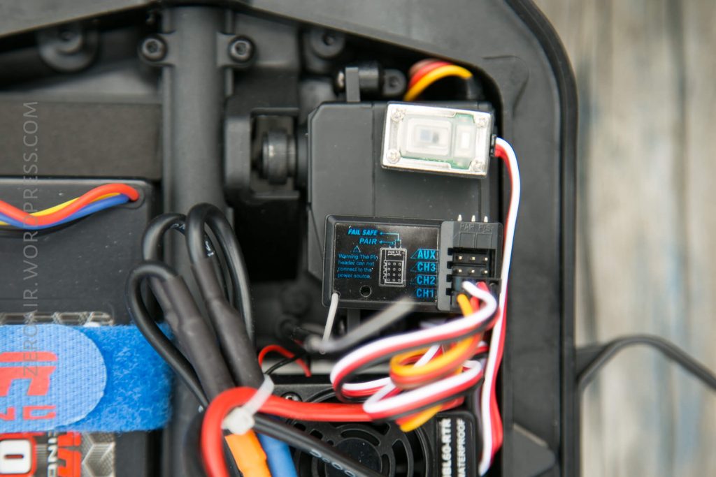 A close-up view of an electronic component inside a device, showing a receiver with labeled ports, several multicolored wires connected, and part of a blue Velcro strap on the left.