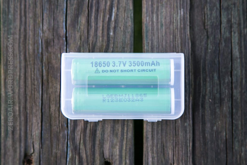 A clear plastic case containing two green 18650 lithium-ion batteries labeled “3.7V 3500mAh” and “Do not short circuit,” placed on a wooden surface.