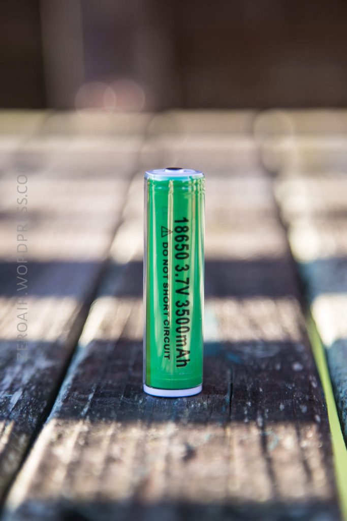A single green lithium-ion battery standing upright on a weathered wooden surface. The label reads 18650 3.7V 3500mAh with additional safety instructions printed below.