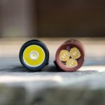 Close-up view of two flashlight heads placed side by side on a wooden surface. The left flashlight has a single LED, while the right one contains four small LEDs arranged in a square pattern.
