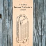 A cardboard box with a line drawing of a lantern on it, labeled zanflare Camping Tent Lantern SB-6039, is shown standing upright on a weathered wooden surface.