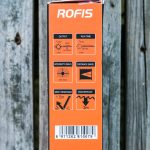 An orange ROFIS flashlight box lists specifications including output, run time, intensity, distance, impact resistance, and waterproof rating, with icons and a barcode below. The box rests on a wooden surface.