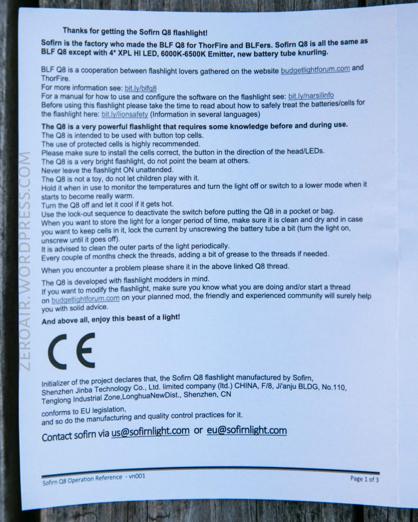 A printed instruction sheet about a Sofirn Q8 flashlight lies on a wooden surface, detailing product features, usage instructions, safety warnings, and contact information for the manufacturer.