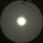 A bright white flashlight beam creates a circular pattern with a defined hotspot and outer spill on a wall. The text ZEROAIR.WORDPRESS.COM appears vertically along the left side.