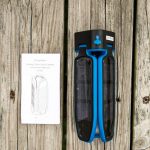 A blue and black folding solar lantern is placed on a wooden surface next to its instruction manual, which shows an illustration of the lantern and includes some printed text.