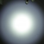 A bright circular beam of white light is projected onto a light-colored wall, creating a halo effect. The text ZEROAIR.WORDPRESS.COM is visible along the left side of the image. Ceiling light fixtures appear in the top right corner.