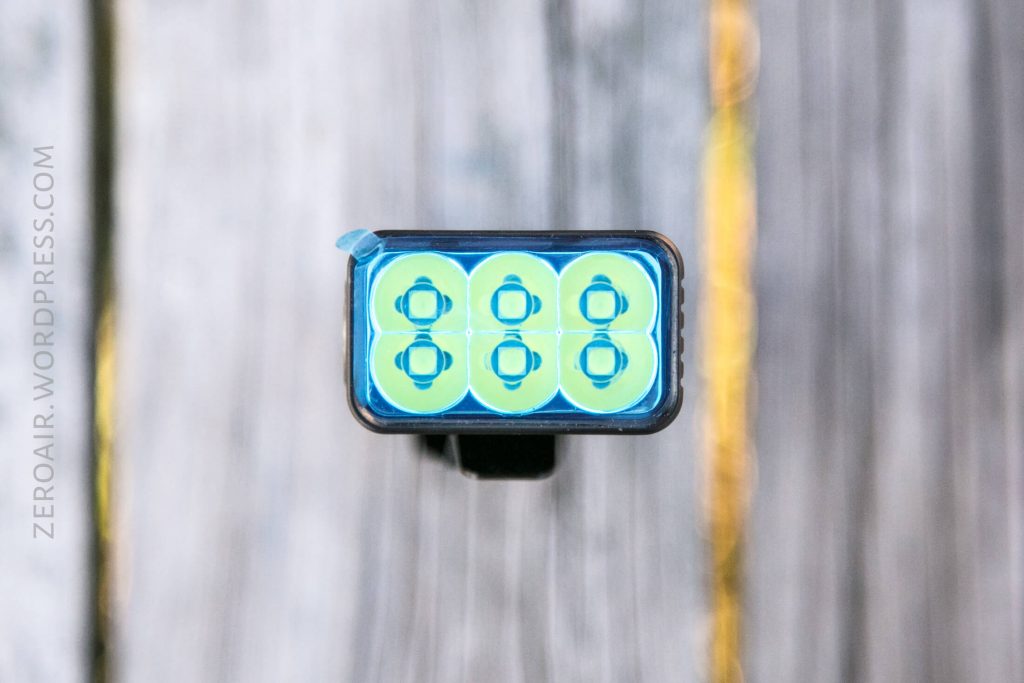 Close-up, top-down view of a rectangular flashlight head with eight circular LED emitters arranged in two rows of four, placed on a wooden surface. The website zeroair.wordpress.com is visible on the left side.