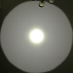 A bright circular beam of light is projected onto a white ceiling, creating a distinct halo effect. Two ceiling light fixtures and the watermark “ZEROAIR.WORDPRESS.COM” are visible on the left side.