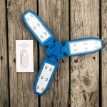 A blue folding LED work light with three open panels and visible LED bulbs is placed on a weathered wooden surface next to an instruction manual.