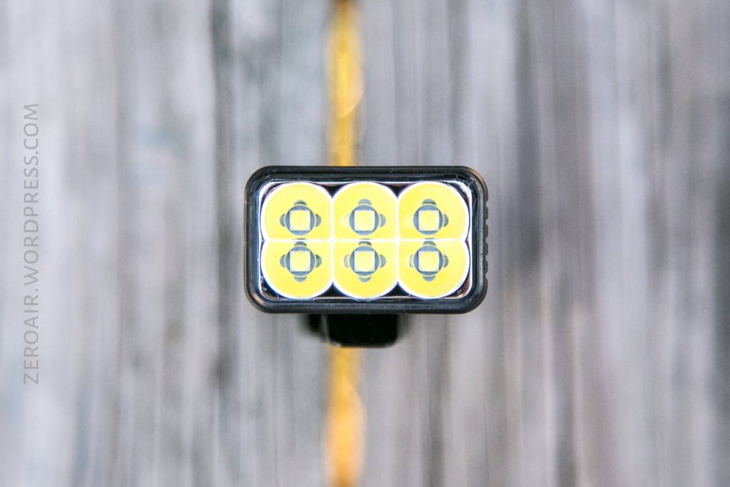 A close-up view of the front of a flashlight with six yellow LED lights arranged in two rows of three, set against a blurred wooden background. The words zeroair.wordpress.com appear on the left side.