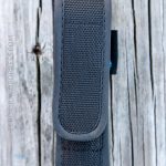 A black nylon pouch with a flap closure is placed vertically on a weathered wooden surface. The pouch appears to be empty and is photographed from above.