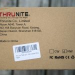 A brown cardboard shipping box displays the ThruNite company logo and address printed in red and black text, along with a barcode label and various certification and handling symbols.