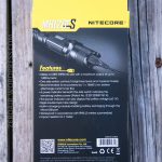 The back of a Nitecore MH12GTS flashlight box features technical specifications, features, and product information text in yellow and white on a black background, with part of the flashlight pictured at the top.