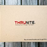 A cardboard box labeled THRUNITE Guiding You Through The Night with a note at the bottom right corner stating Buy at www.thrunite.com to get 5% off, placed on a wooden surface.