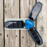 A blue, three-panel solar charger with the brand name zanflare sits open on a wooden surface next to a US one-dollar bill for scale.