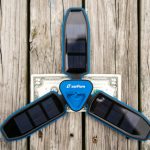 A blue, three-panel solar charger labeled zanflare is displayed open on a weathered wooden surface, with a two-dollar bill placed underneath the center for scale.