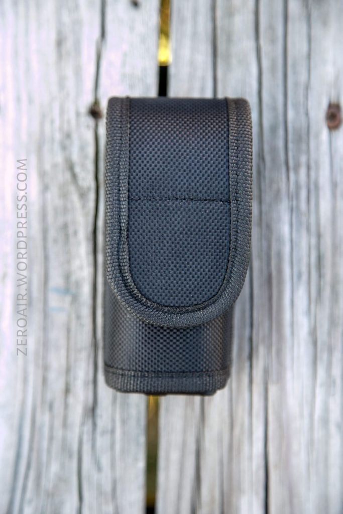 A black textured nylon pouch with a flap is shown standing upright on a weathered wooden surface. The text zeroair.wordpress.com is faintly visible along the left side of the image.