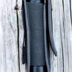 A black cylindrical object in a black fabric case with a Velcro flap, placed vertically on a weathered wooden surface. The case features a metal D-ring on the left. The text ZEROAIR.WORDPRESS.COM appears on the left.