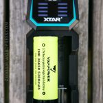 A yellow rechargeable lithium-ion battery labeled VAPPOWER IMR 26650 5200mAh is placed in a black XTAR D2 battery charger, photographed from above on a wooden surface.