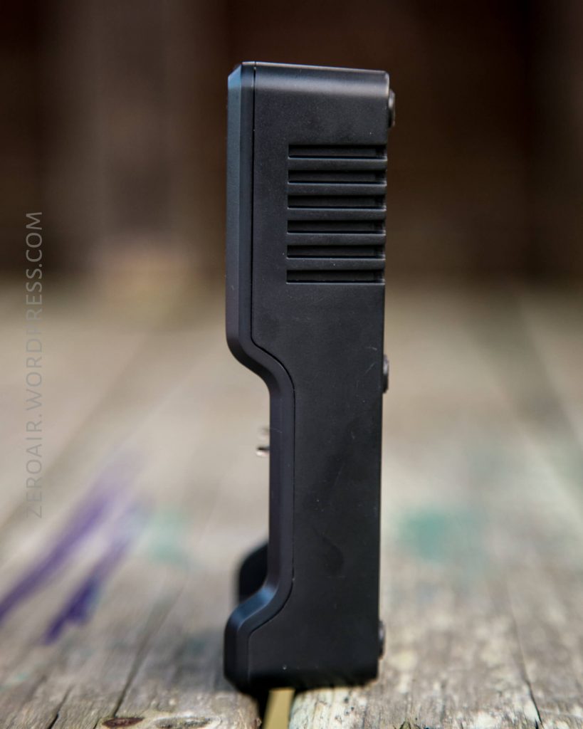 A black rectangular electronic device, possibly a battery charger, standing upright on a wooden surface with a blurred background.