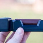 A hand holds a black battery charger with a cylindrical brown battery labeled “18650” inserted. The background is blurred; zeroair.wordpress.com is faintly visible along the left side.