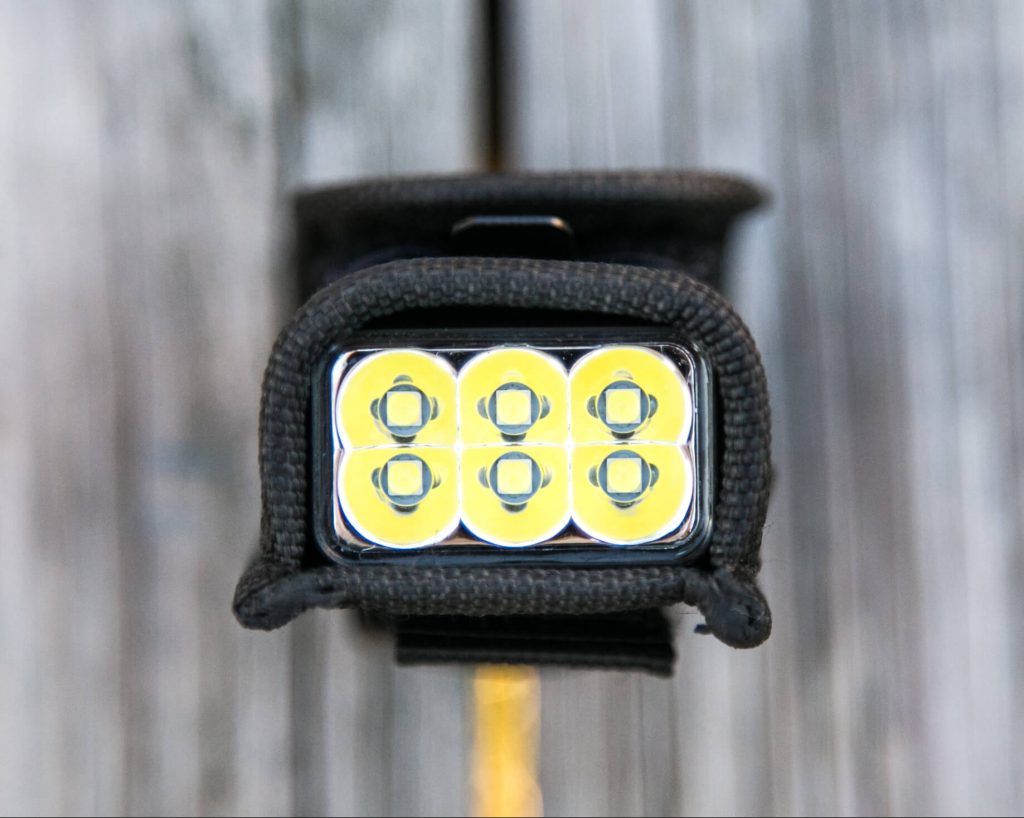 Close-up view of a rectangular flashlight with six round LED bulbs arranged in two rows of three, encased in a black protective cover, placed on a wooden surface.