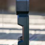 A close-up, side view of a black electronic device with a rectangular shape and angular contours, placed upright on a wooden surface with a blurred background.